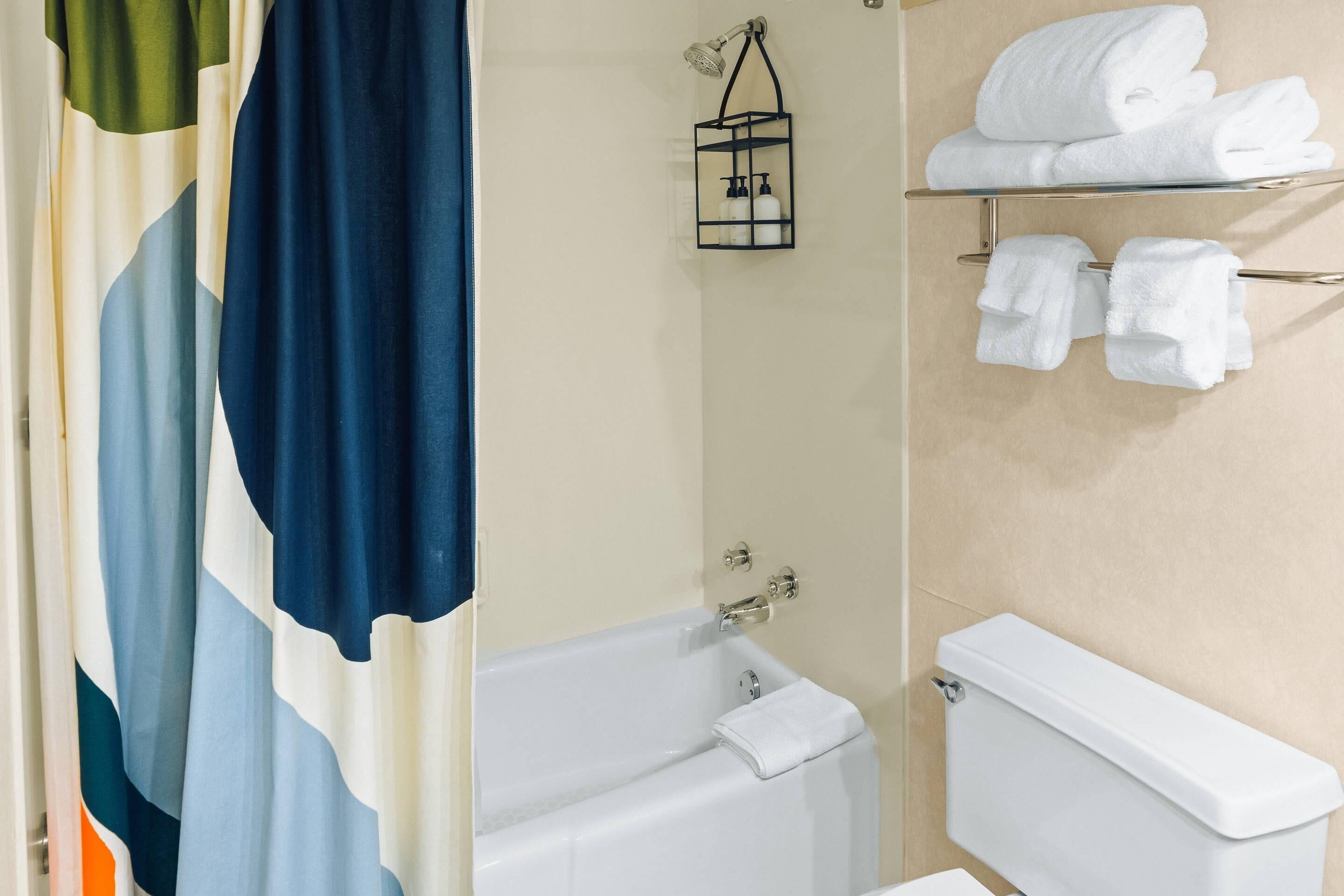A bathroom with a bathtub, a toilet, and a towel rack with folded towels.