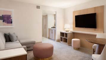 Een moderne woonkamer met een bank, een voetenbankje en een aan de muur bevestigde televisie.