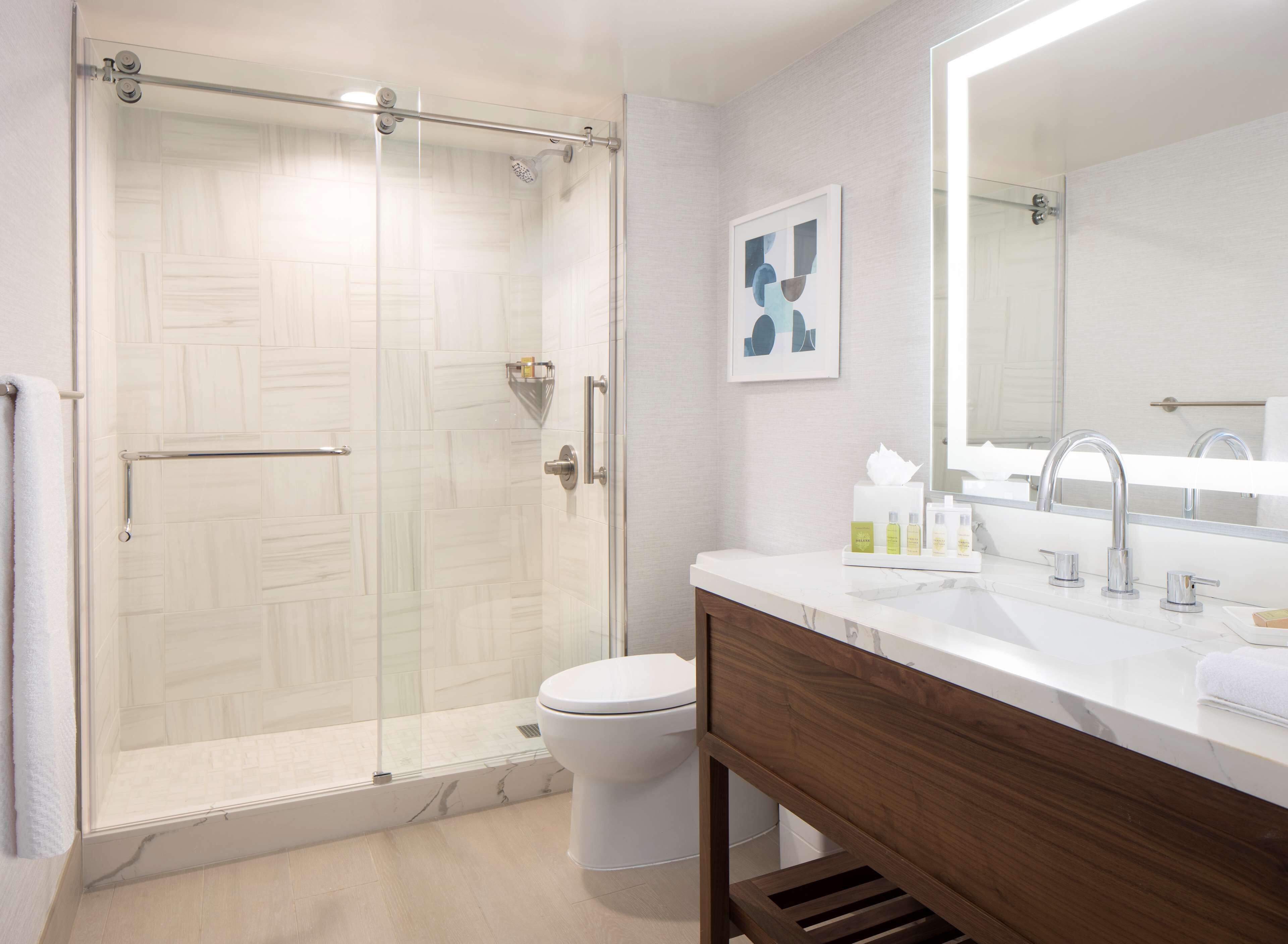 A modern bathroom with a glass-enclosed shower, a white toilet, a wooden vanity with a marble countertop, and a large mirror.