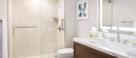 A modern bathroom with a glass-enclosed shower, a white toilet, a wooden vanity with a marble countertop, and a large mirror.