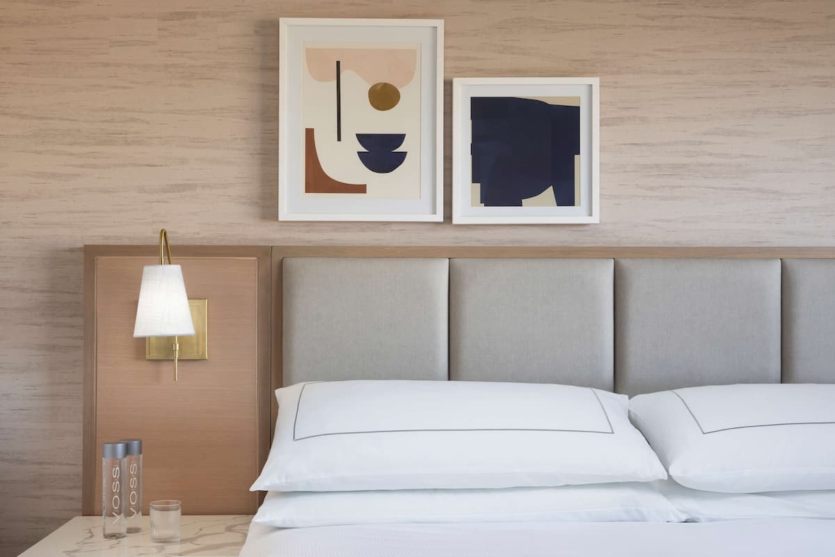 A hotel room with a bed, a nightstand with a lamp, and two framed abstract artworks on the wall.