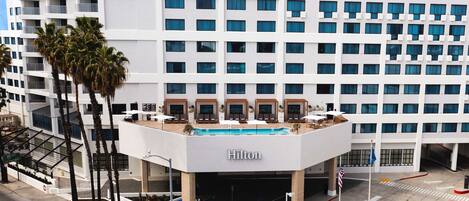 Un hôtel moderne doté d’une piscine sur le toit, de palmiers et offrant une vue sur un ciel dégagé.