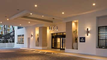 A modern hotel entrance with a revolving door, potted plants, and a sign indicating it's a Hilton property.