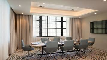 A conference room with a large table, six chairs, and a large window with curtains.