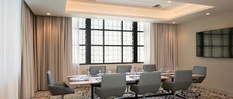 A conference room with a large table, six chairs, and a large window with curtains.