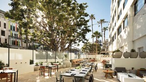 An outdoor dining area with tables and chairs, surrounded by large potted plants and trees. - Hilton Santa Monica Hotel & Suites (Santa Monica)