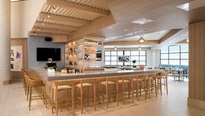 A modern kitchen with a central island, bar stools, and a dining area with tables and chairs. - Hilton Santa Monica Hotel & Suites (Santa Monica)