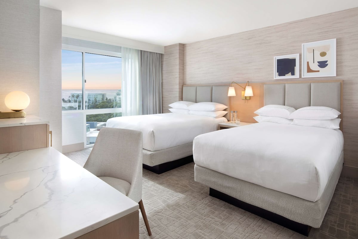 A hotel room with two beds, a desk, and a view of the city.