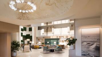 A spacious, modern lobby with a high ceiling, a central seating area, and a large painting on the right wall.