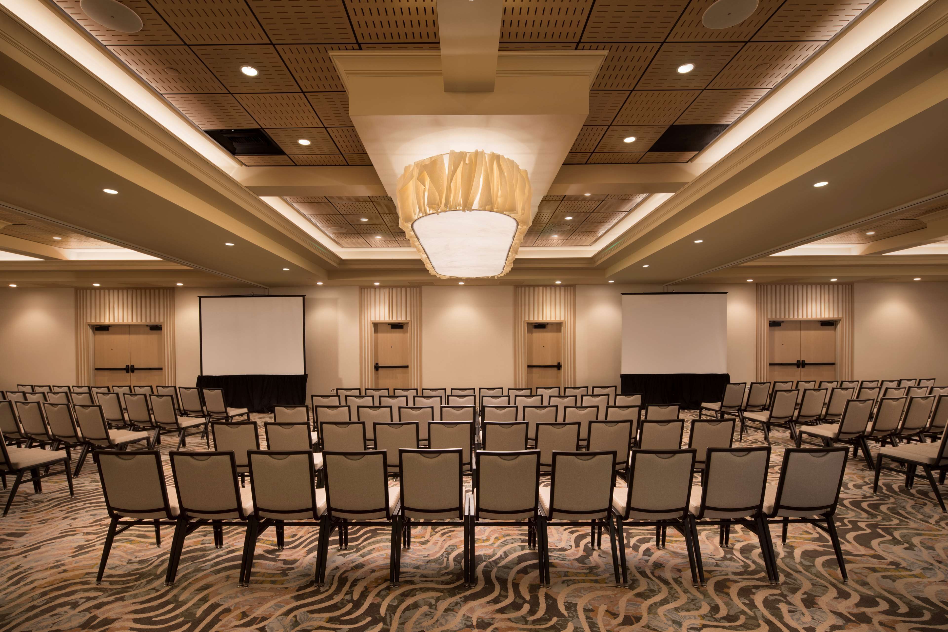 A conference room with rows of chairs, a large screen, and a ceiling with recessed lighting.