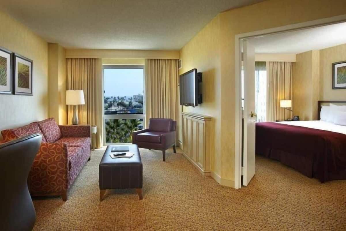 A hotel room with a sofa, armchair, ottoman, television, and a bed.