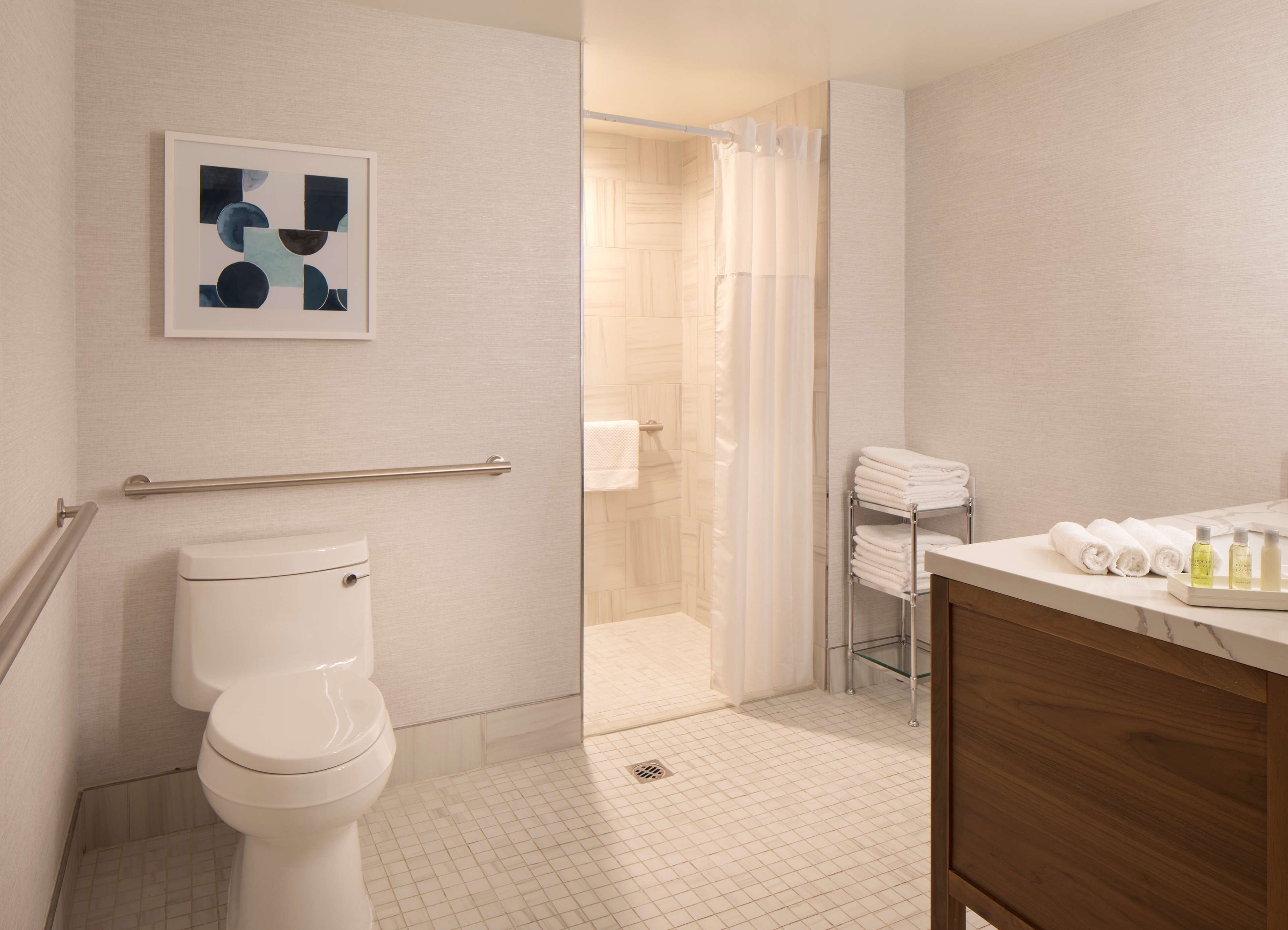 A modern bathroom with a toilet, a glass shower enclosure, a towel rack with folded towels, and a sink area with toiletries.