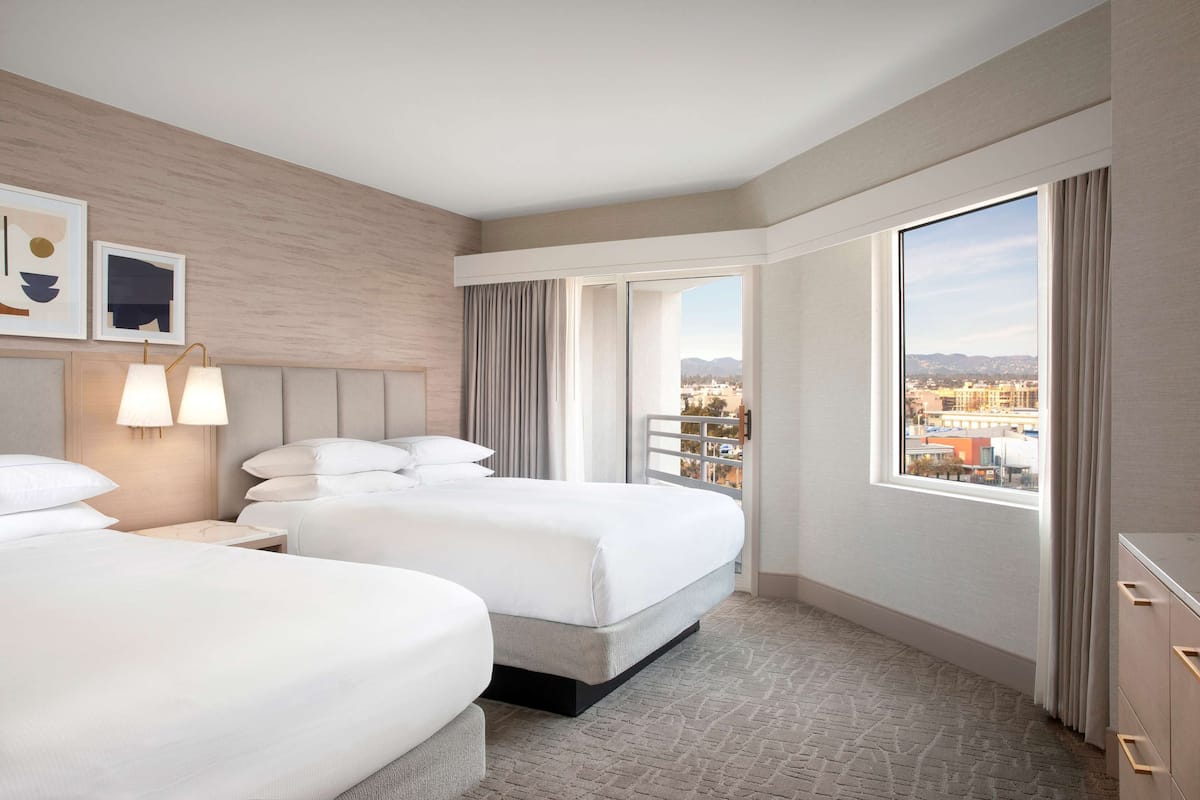 A hotel room with two beds, a large window with a city view, and a modern design.