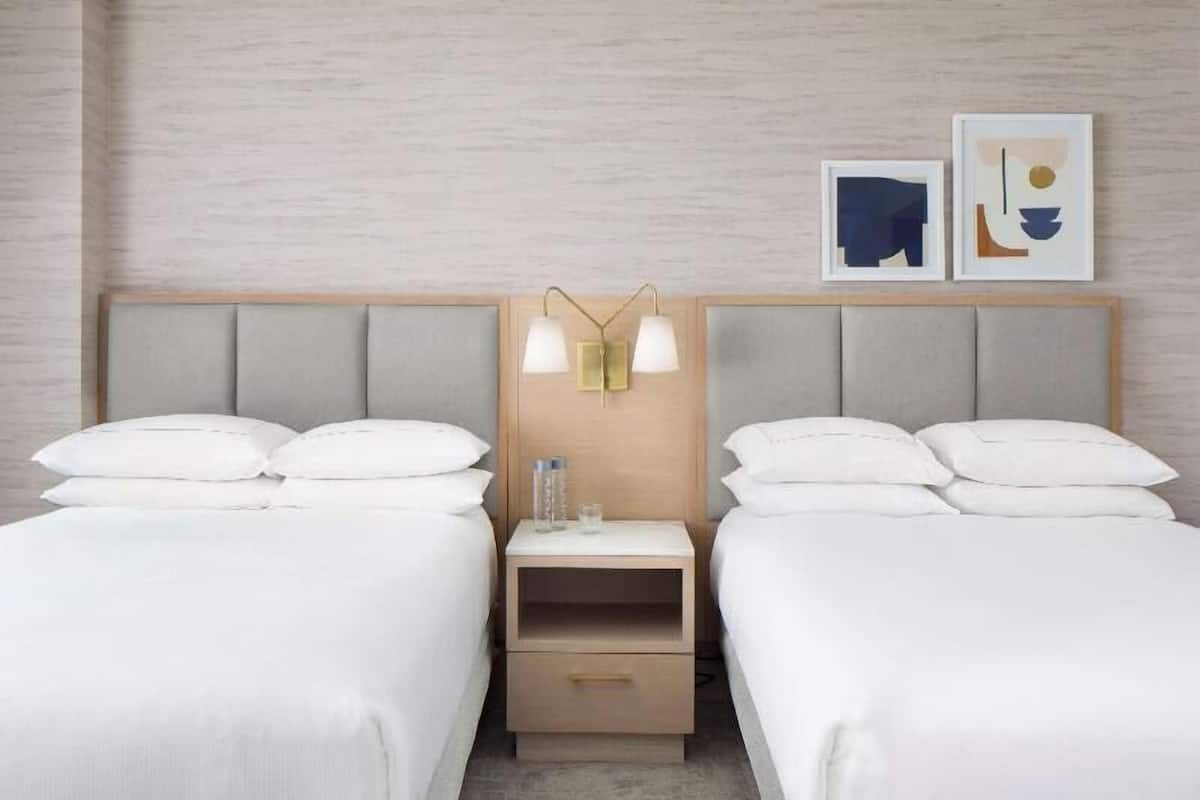 A hotel room with two beds, a nightstand with a lamp, and artwork on the wall.