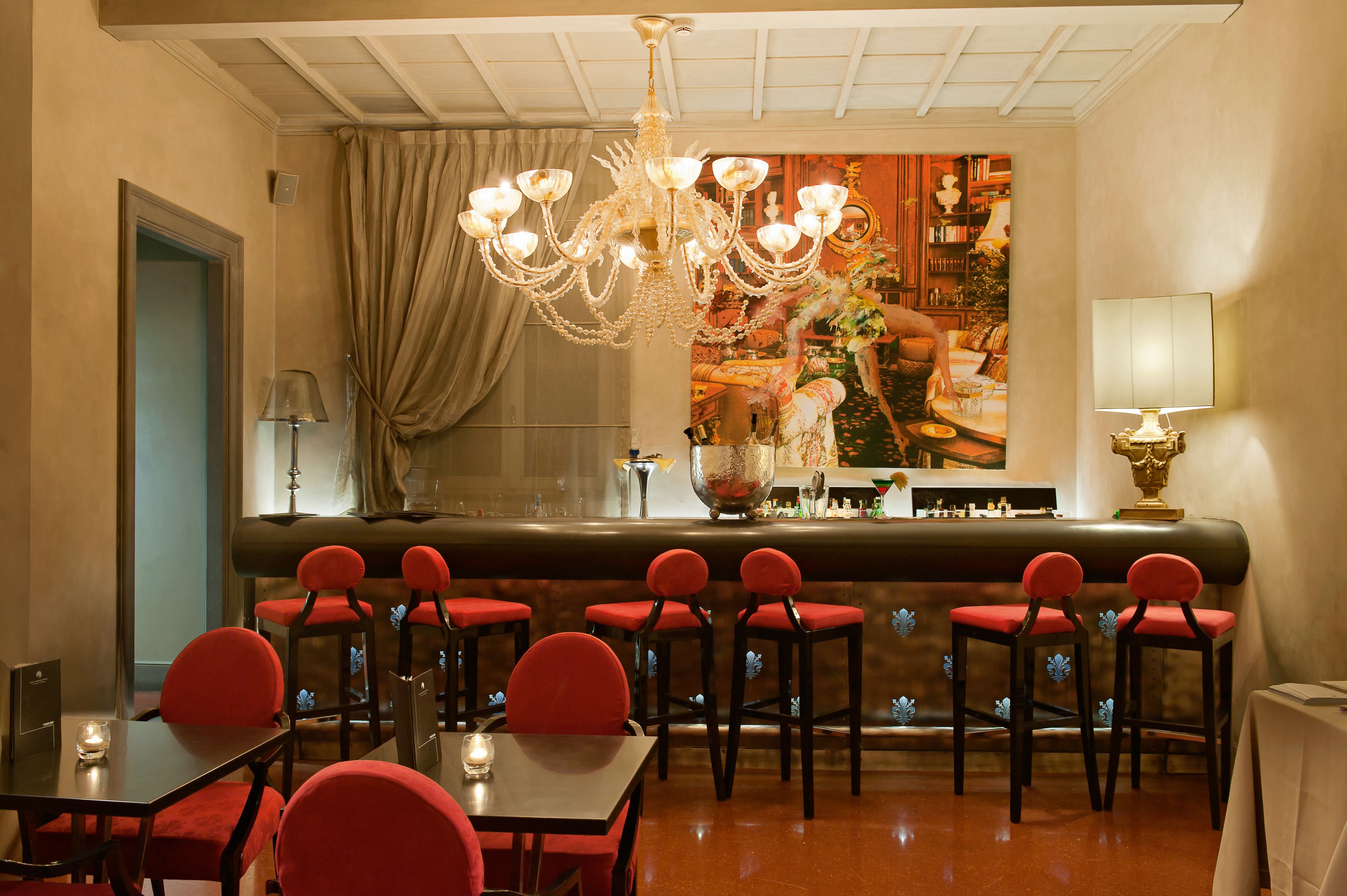 Un restaurante con zona de bar, sillas tapizadas de rojo, una lámpara de araña y un espejo decorativo grande.