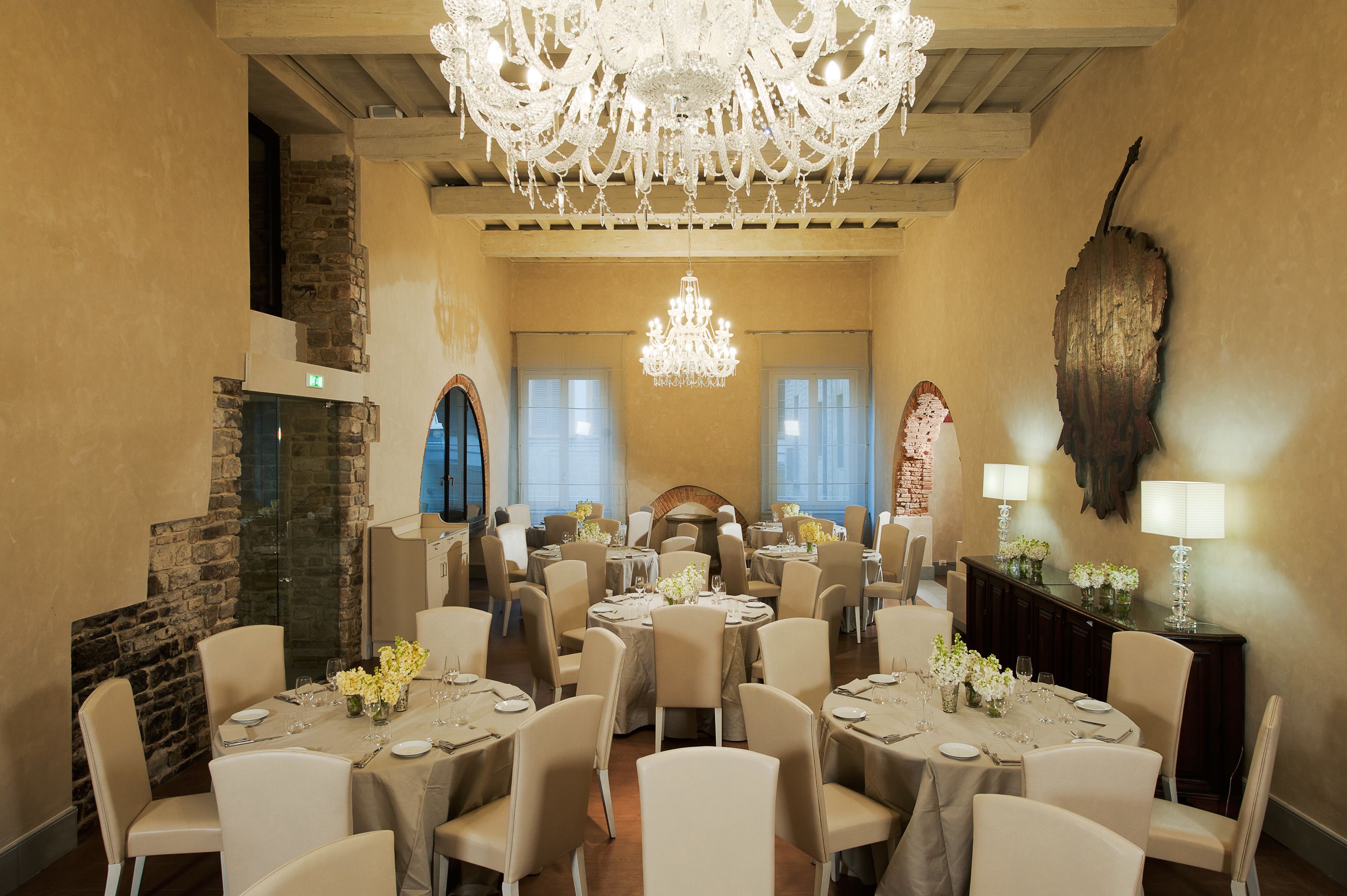 A spacious dining area with round tables, beige chairs, and a large chandelier.