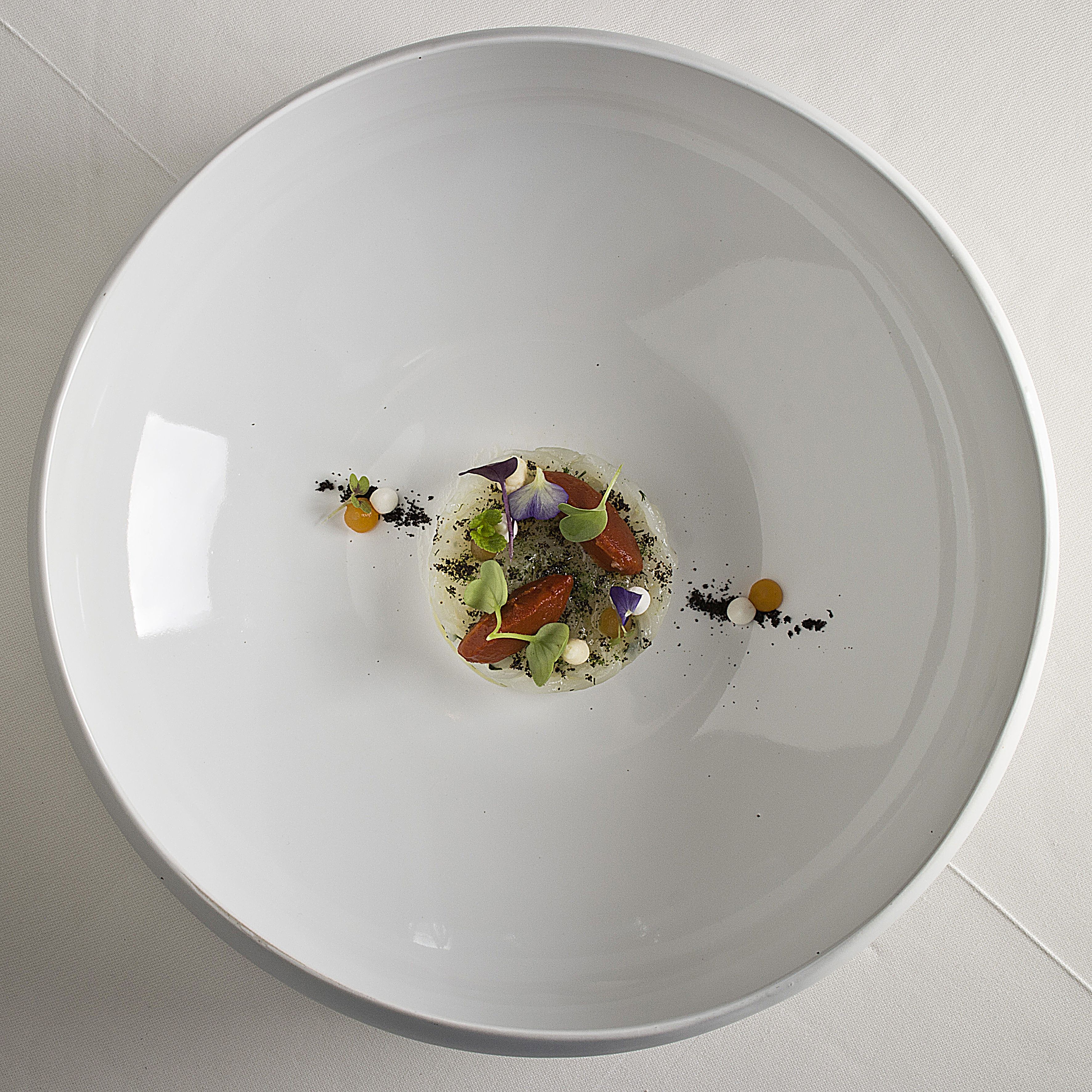 Een wit bord met een centrale garnering en losse, eetbare bloemen.