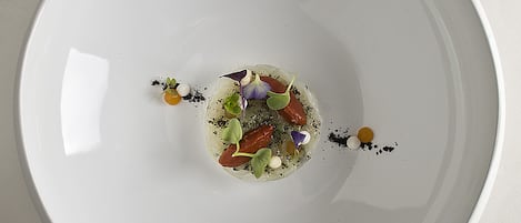 Een wit bord met een centrale garnering en losse, eetbare bloemen.