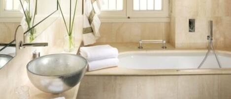 A bathroom with a large bathtub, a glass bowl, and towels.