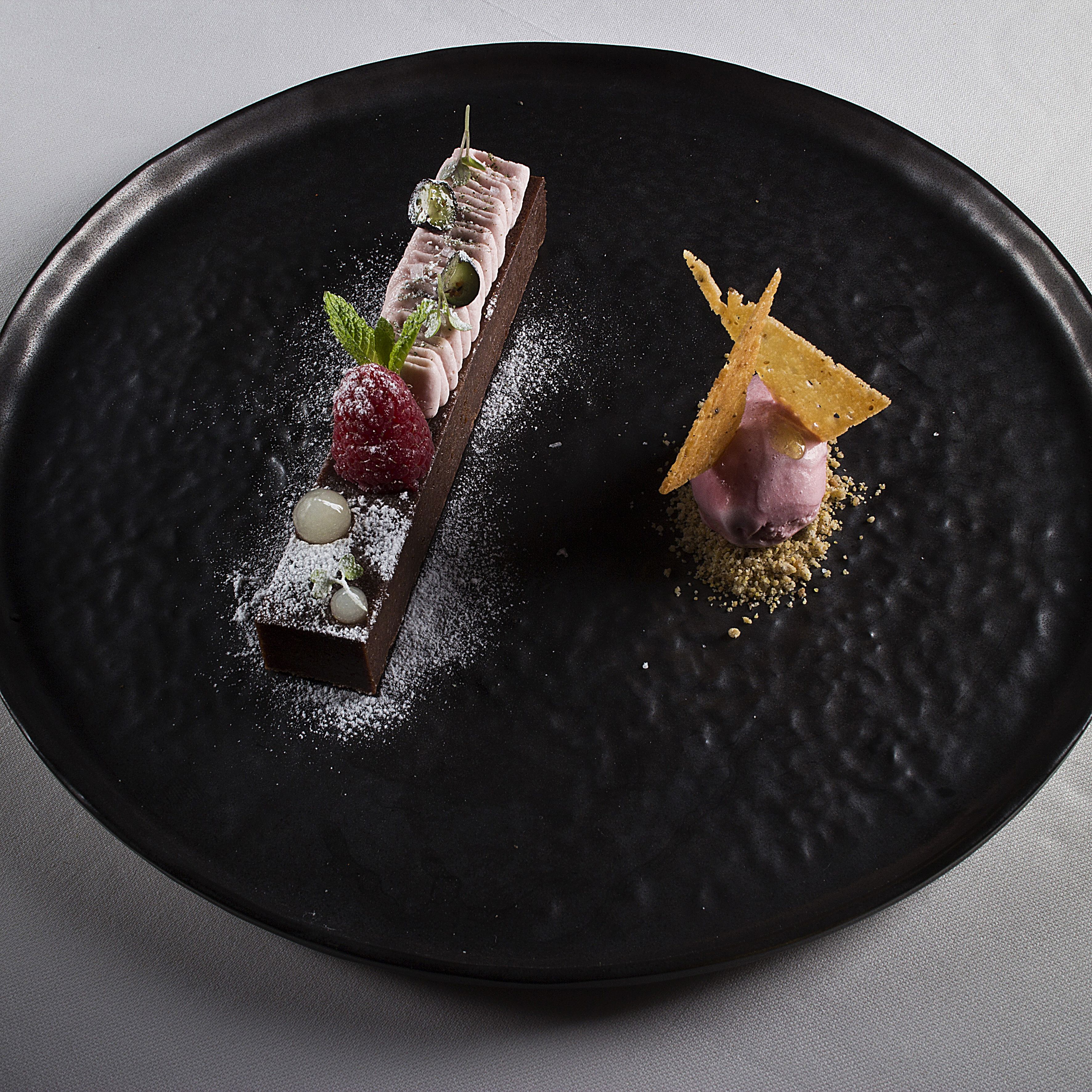 A dessert on a black plate with various garnishes.