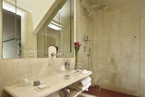 A modern bathroom with a glass bowl sink, a large mirror, and a glass-enclosed shower.