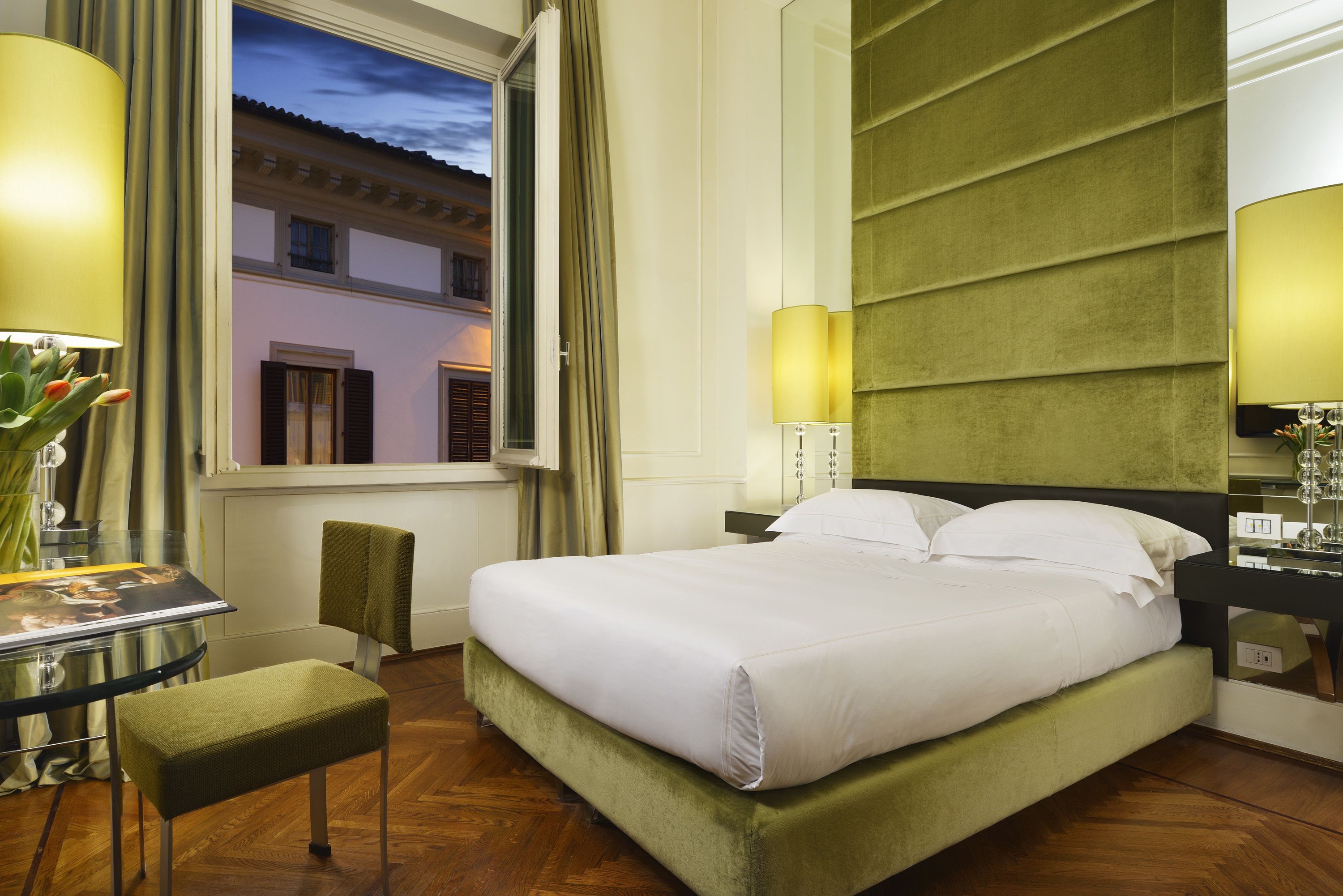 Una habitación de hotel con cama, escritorio, silla y ventana con cortinas.