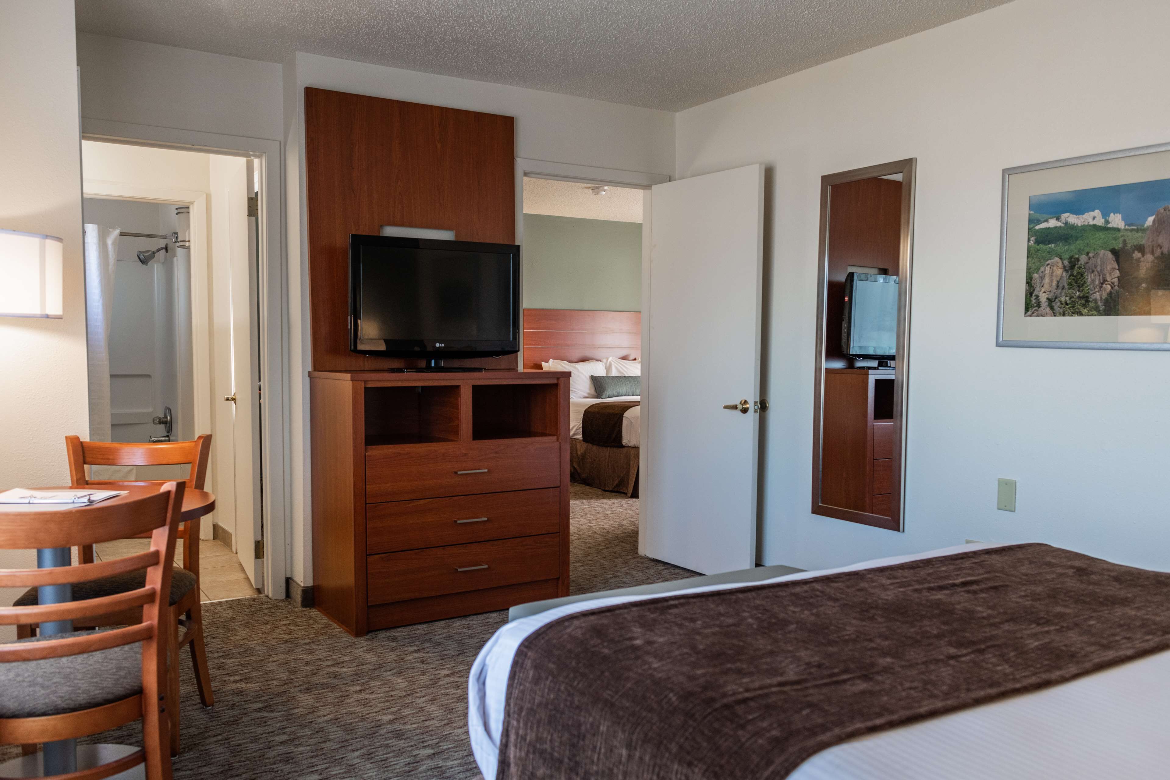 Ein Hotelzimmer mit einem Bett, einer Holzkommode mit Fernseher, einem Schreibtisch mit Stühlen und einer Tür zu einem Badezimmer.