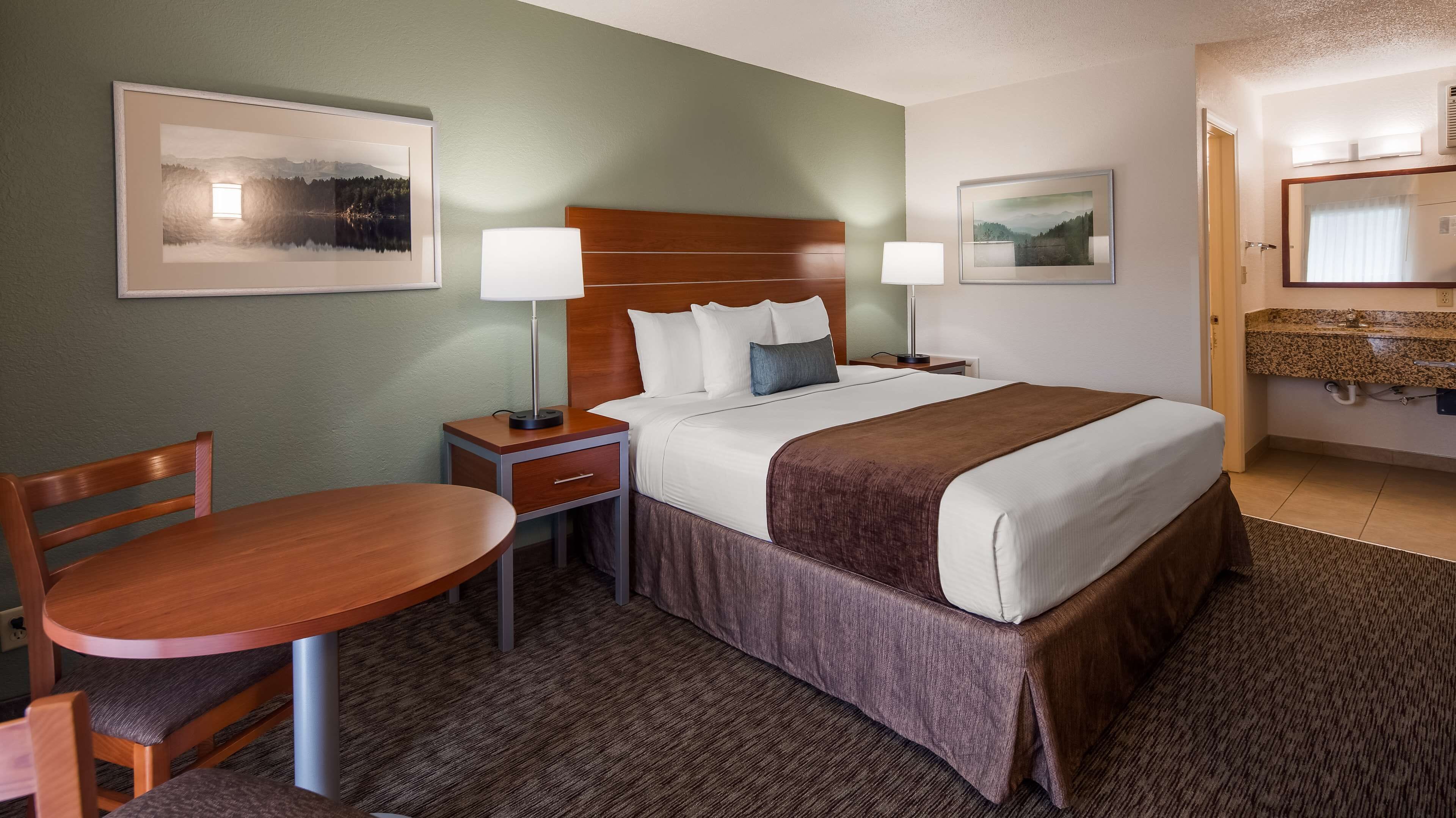 A hotel room with a bed, bedside tables, a desk, and chairs.