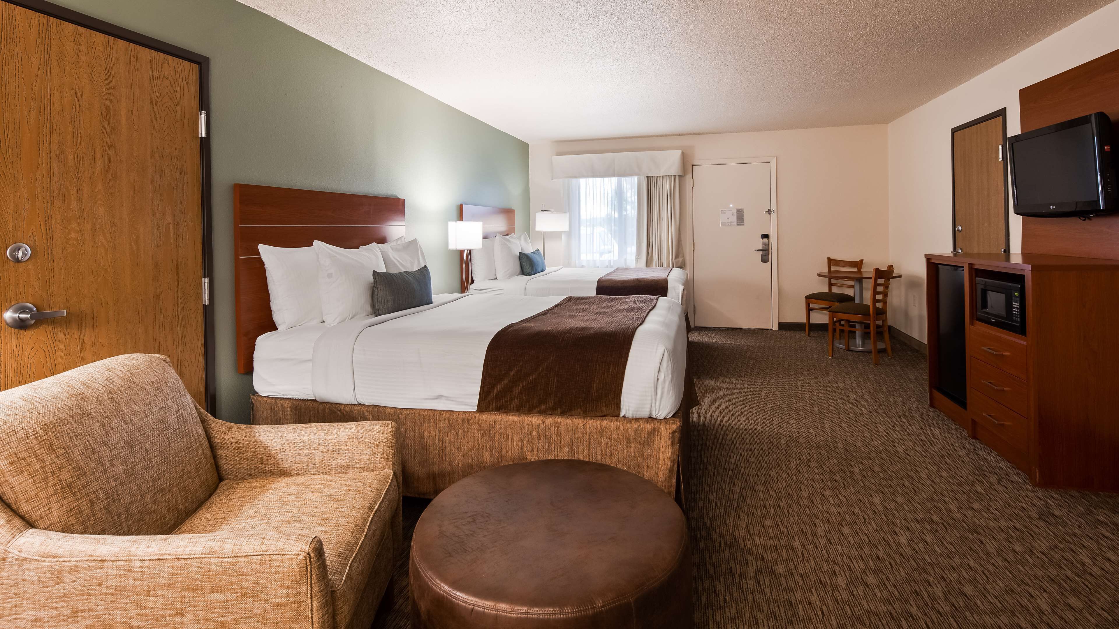 A hotel room with a large bed, a chair, a small table, a television, and a microwave.