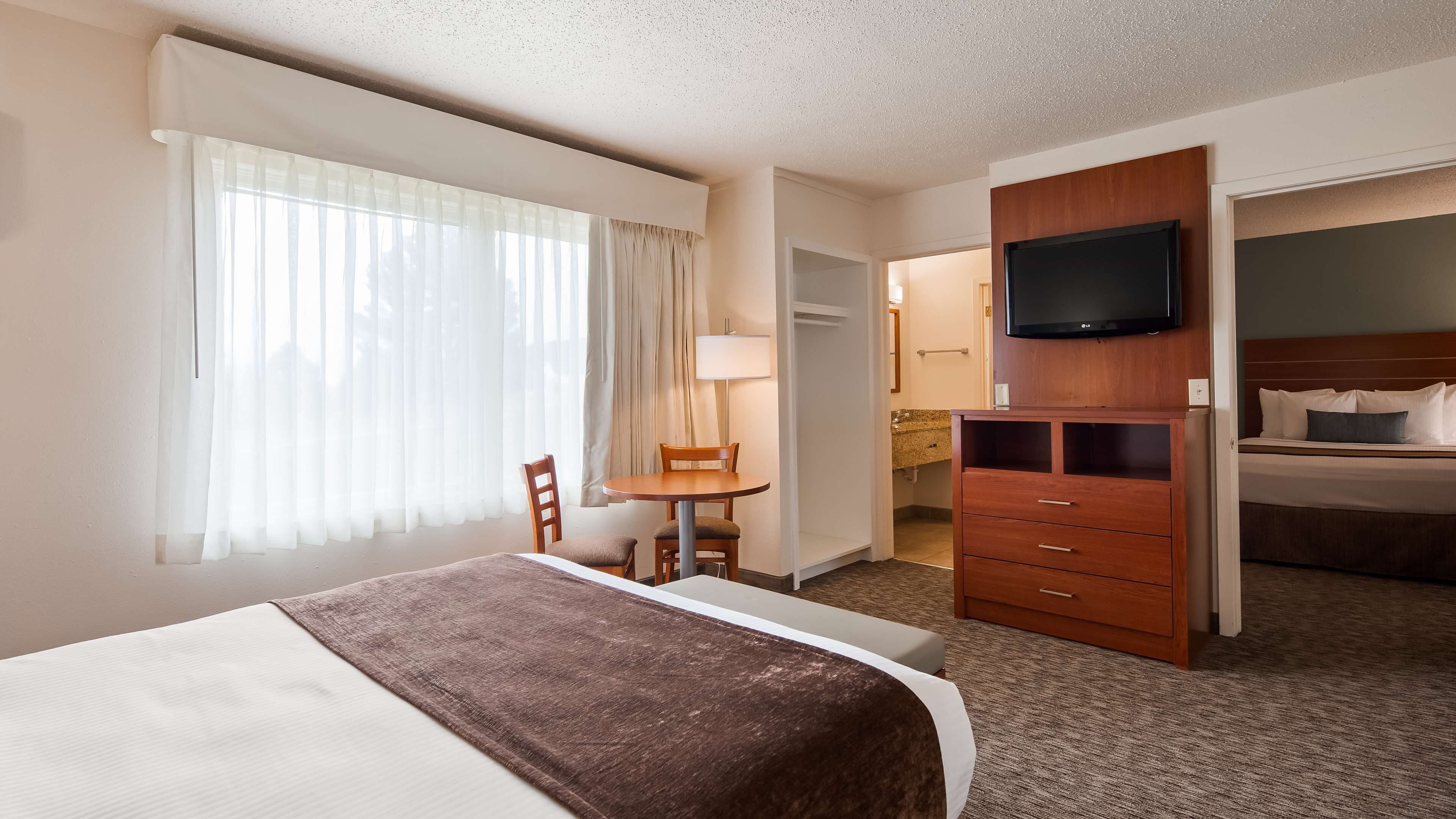 A hotel room with a bed, a desk, a chair, a TV, and a wardrobe.