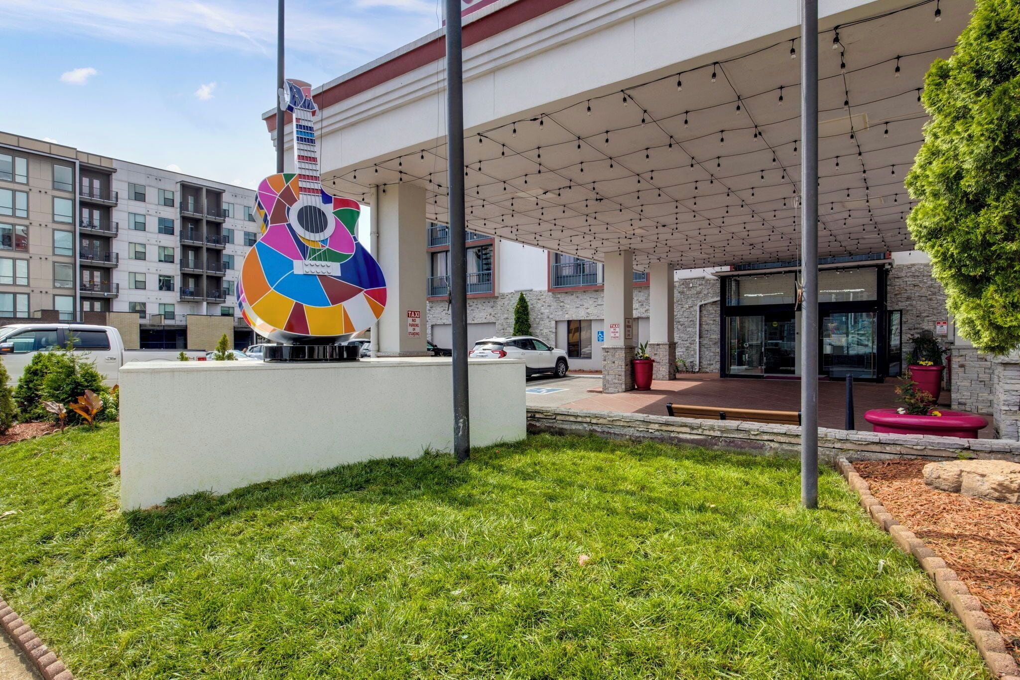 Un edificio con una escultura de guitarra de colores en la fachada, un acceso cubierto y un área de estacionamiento.