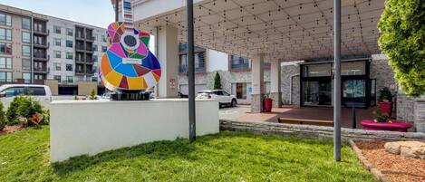 Un edificio con una escultura de guitarra de colores en la fachada, un acceso cubierto y un área de estacionamiento.
