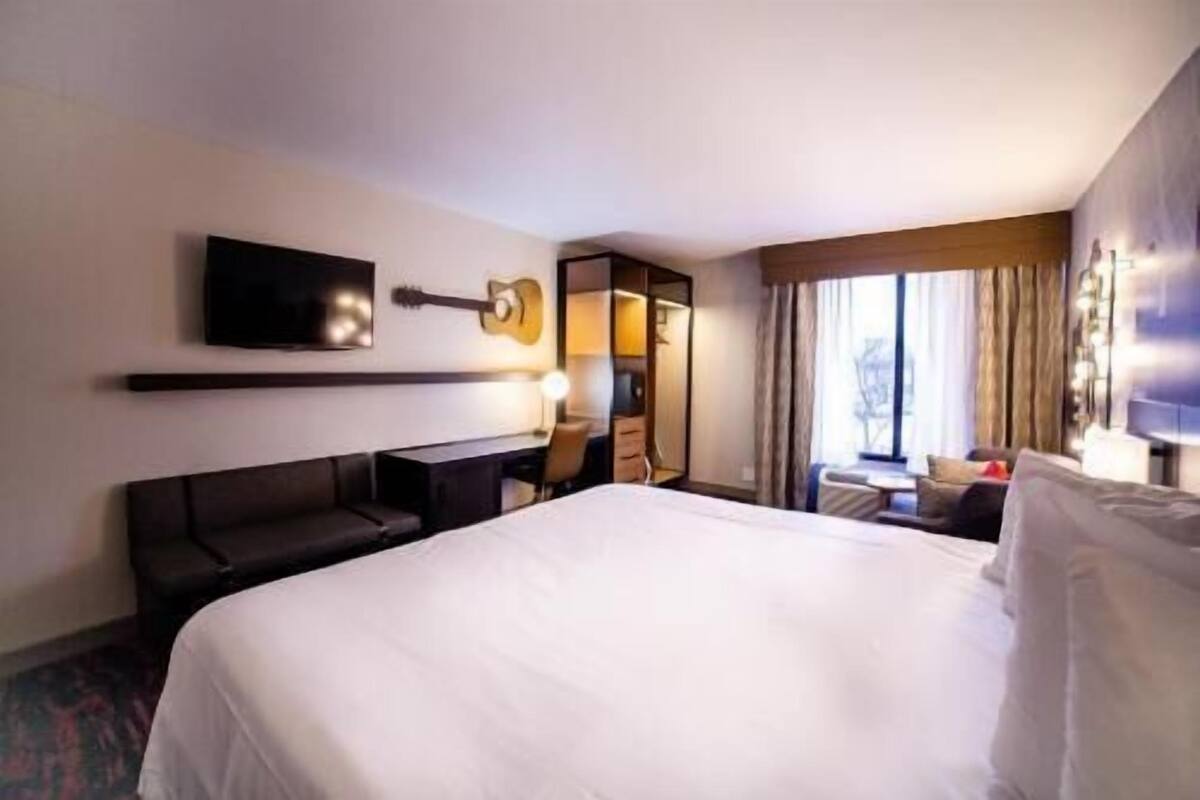 A hotel room with a large bed, a desk, a chair, a TV, and a window with curtains.