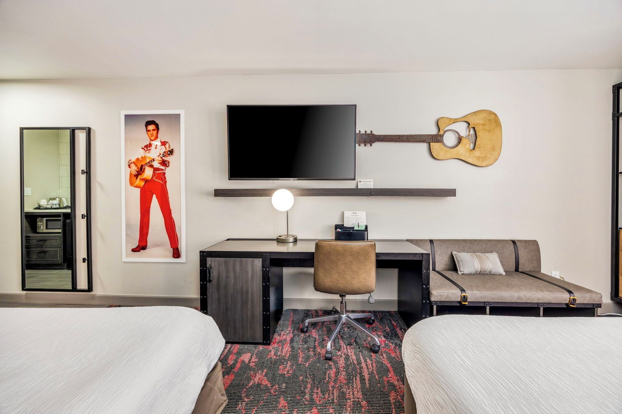 Camera d'albergo con due letti, una scrivania con una TV a schermo piatto, una chitarra, un poster e uno specchio.