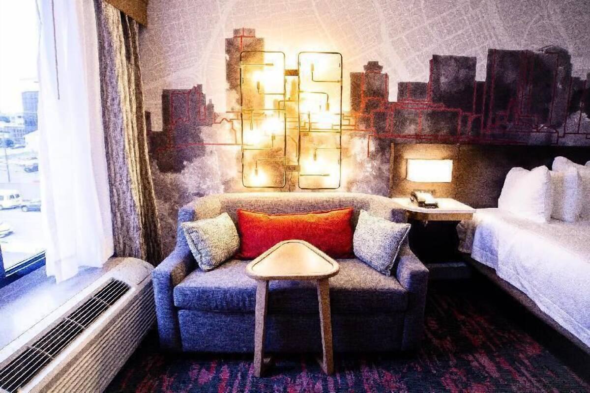 A hotel room with a sofa, a small table, a lamp, and a bed.