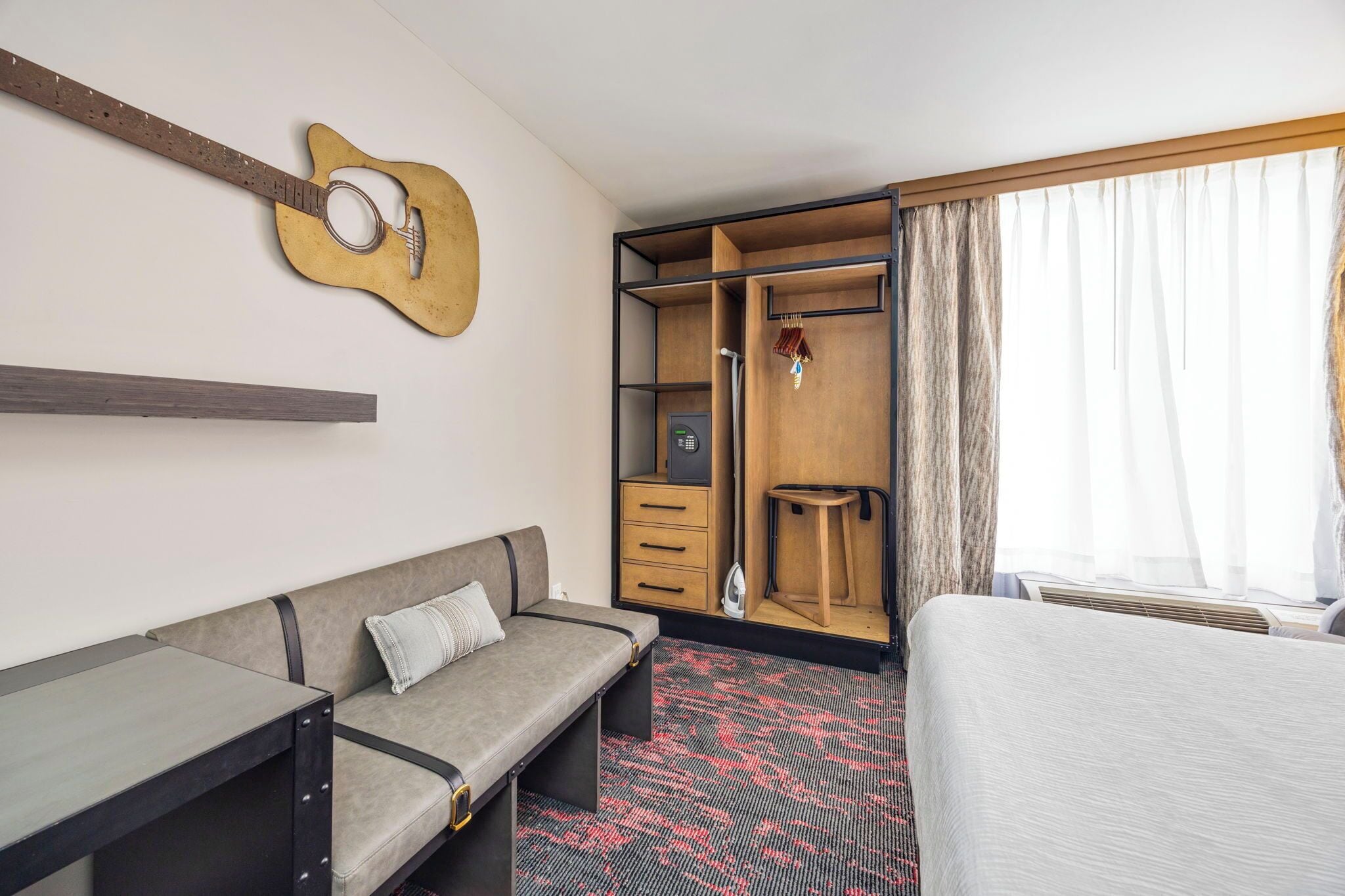 Hotellihuone, jossa on sänky, sohva, työpöytä, vaatekaappi ja kitara seinällä.