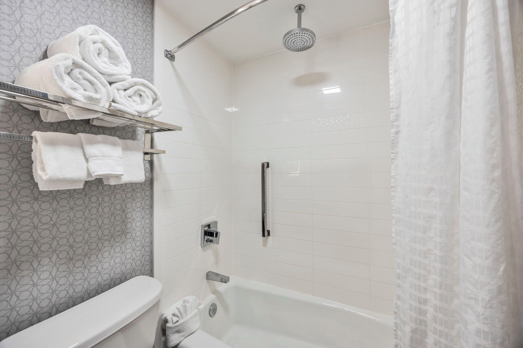 Een moderne badkamer met een douche, toilet en een handdoekrek met netjes opgerolde handdoeken.
