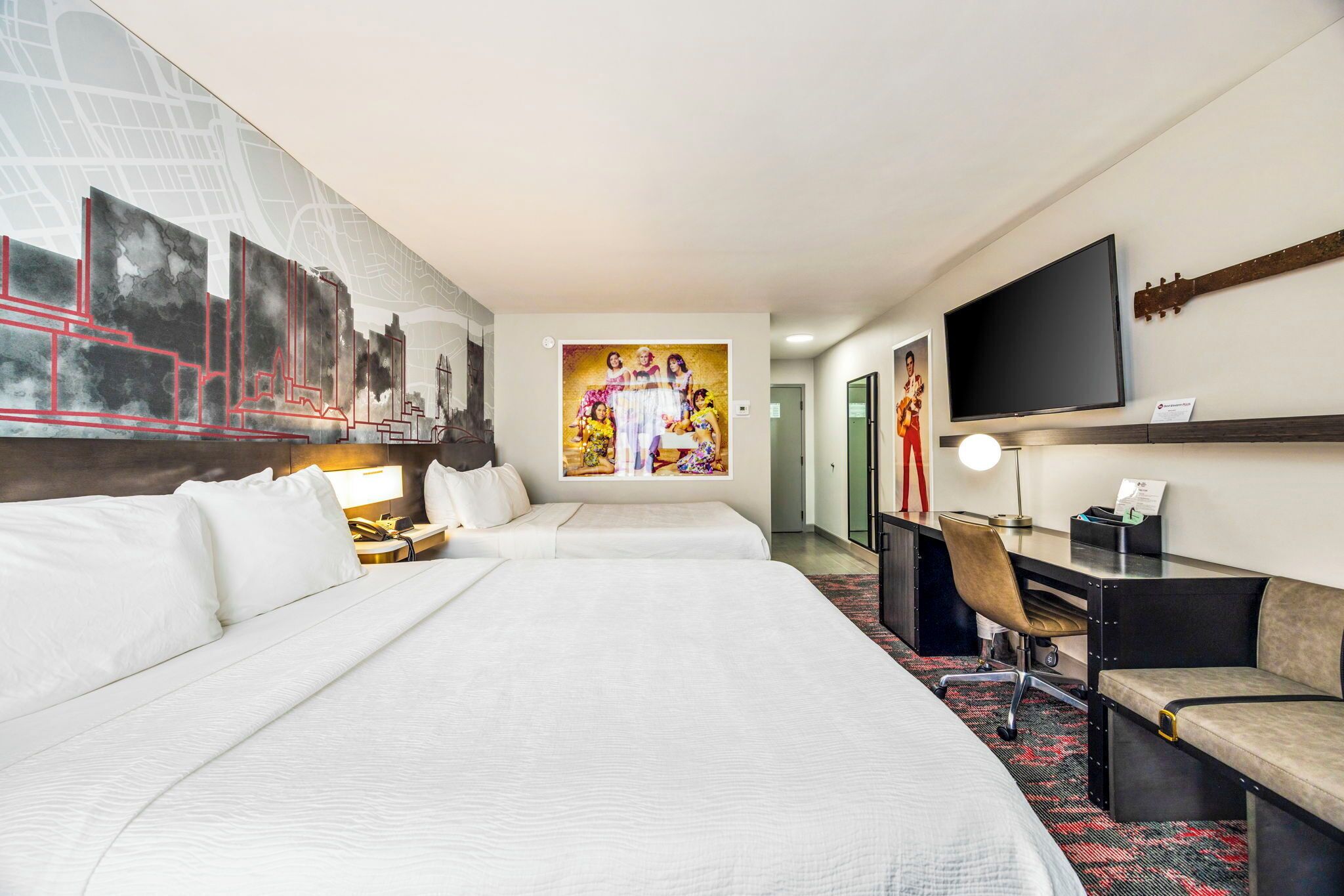 A hotel room with two beds, a desk, a chair, a television, and a large painting on the wall.