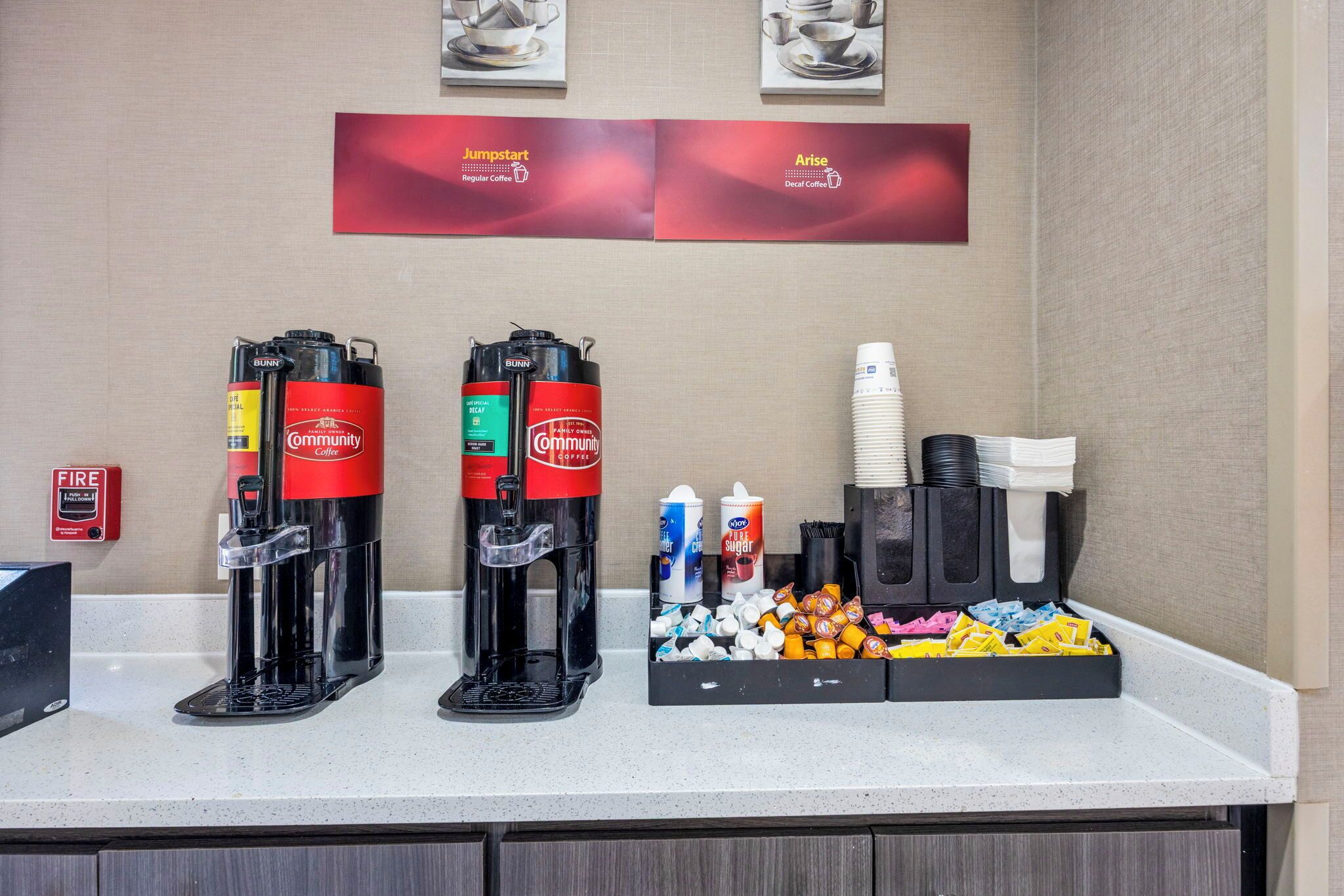 Un espace dédié au café, comprenant deux machines à café, un détecteur d’incendie et divers accessoires liés au café, le tout disposé sur un comptoir.