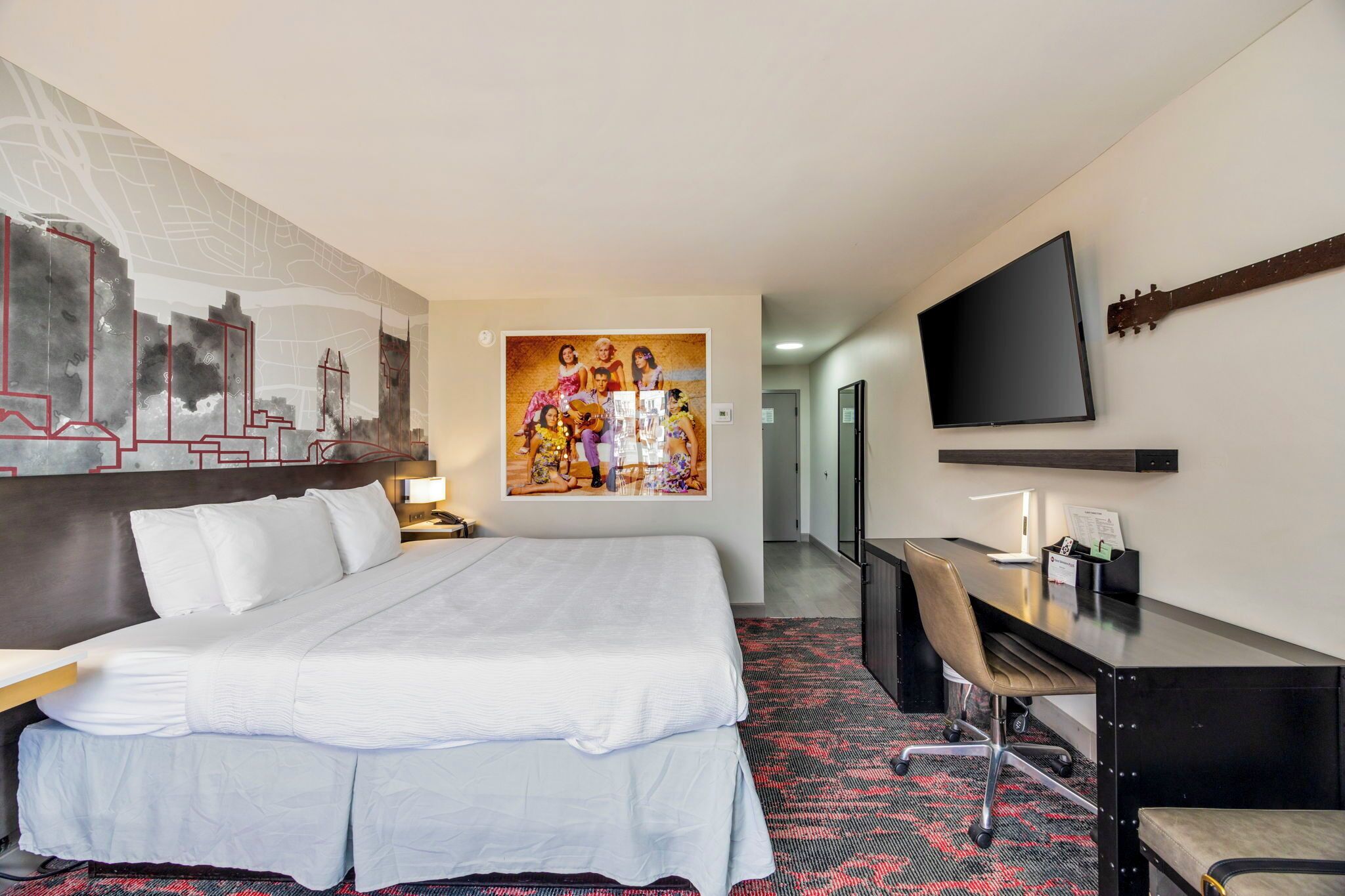 A hotel room with a large bed, a desk with a chair, a television, and a painting on the wall.