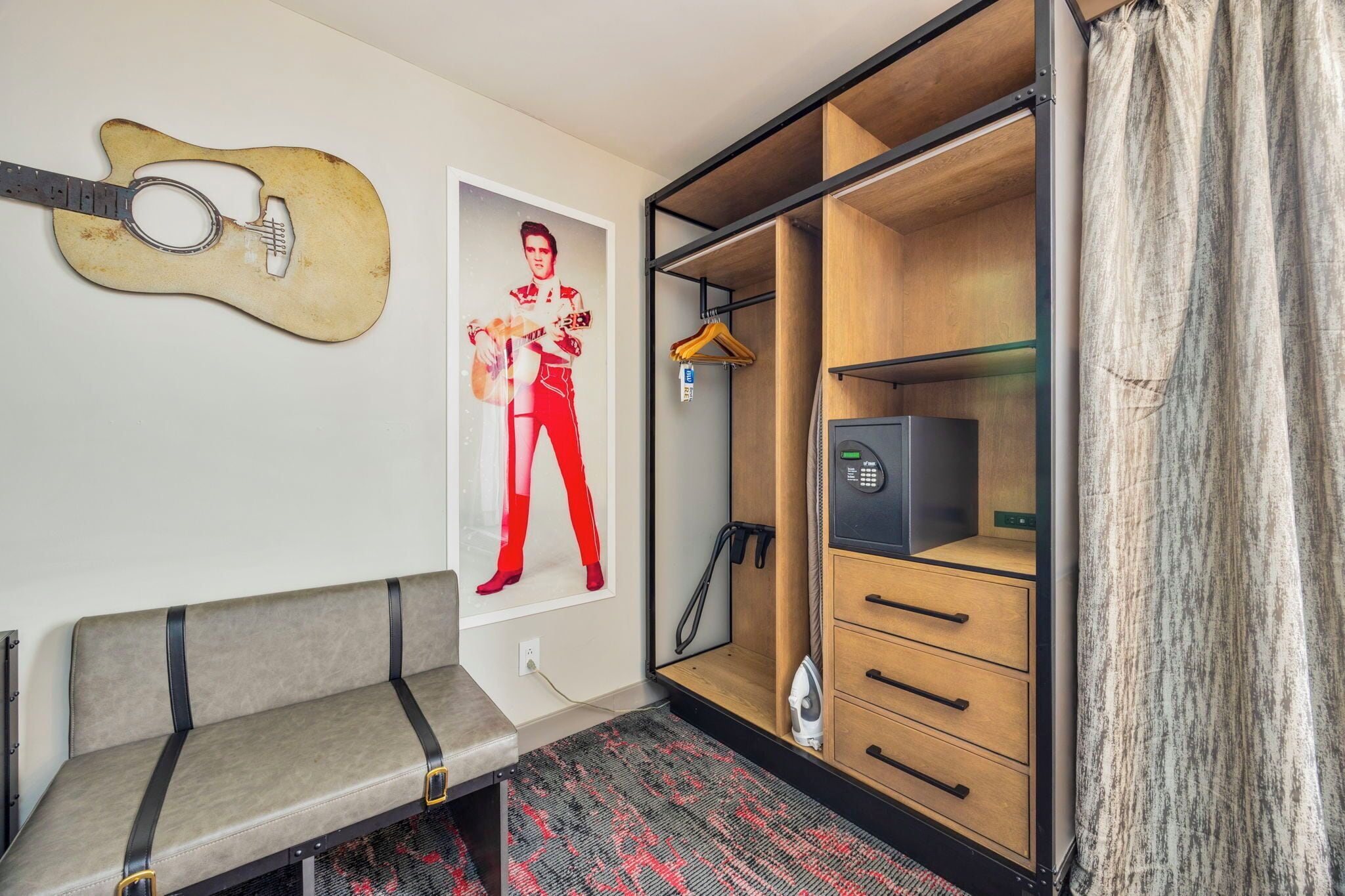 Hotelkamer met een bank, een gitaar decoratie, een poster, een kledingkast en een stofzuiger.