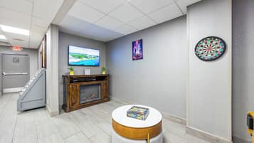 Un hall d’entrée moderne doté d’un téléviseur à écran plat, d’un jeu de fléchettes, d’un tableau et d’une petite table ronde sur laquelle est posé un livre.