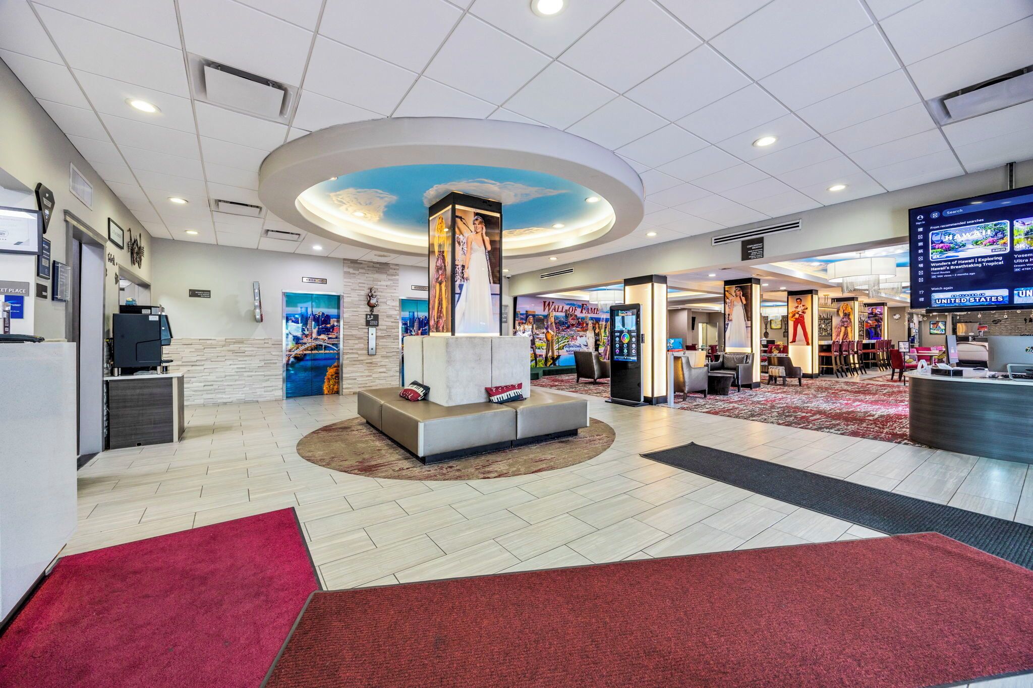 A hotel lobby with a reception desk, seating area, and a large digital screen displaying content.