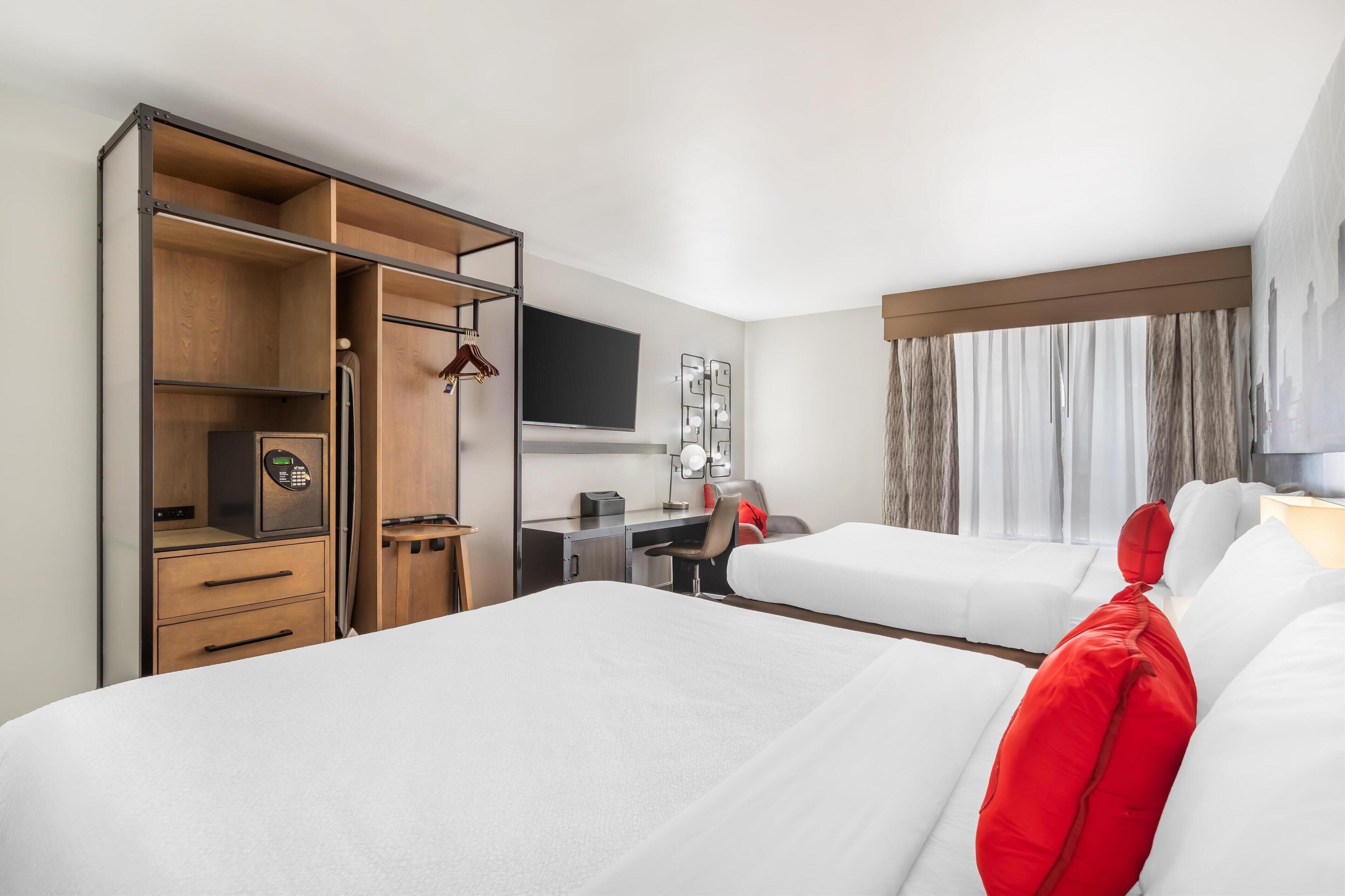 A hotel room with two beds, a desk, a wardrobe, and a TV.
