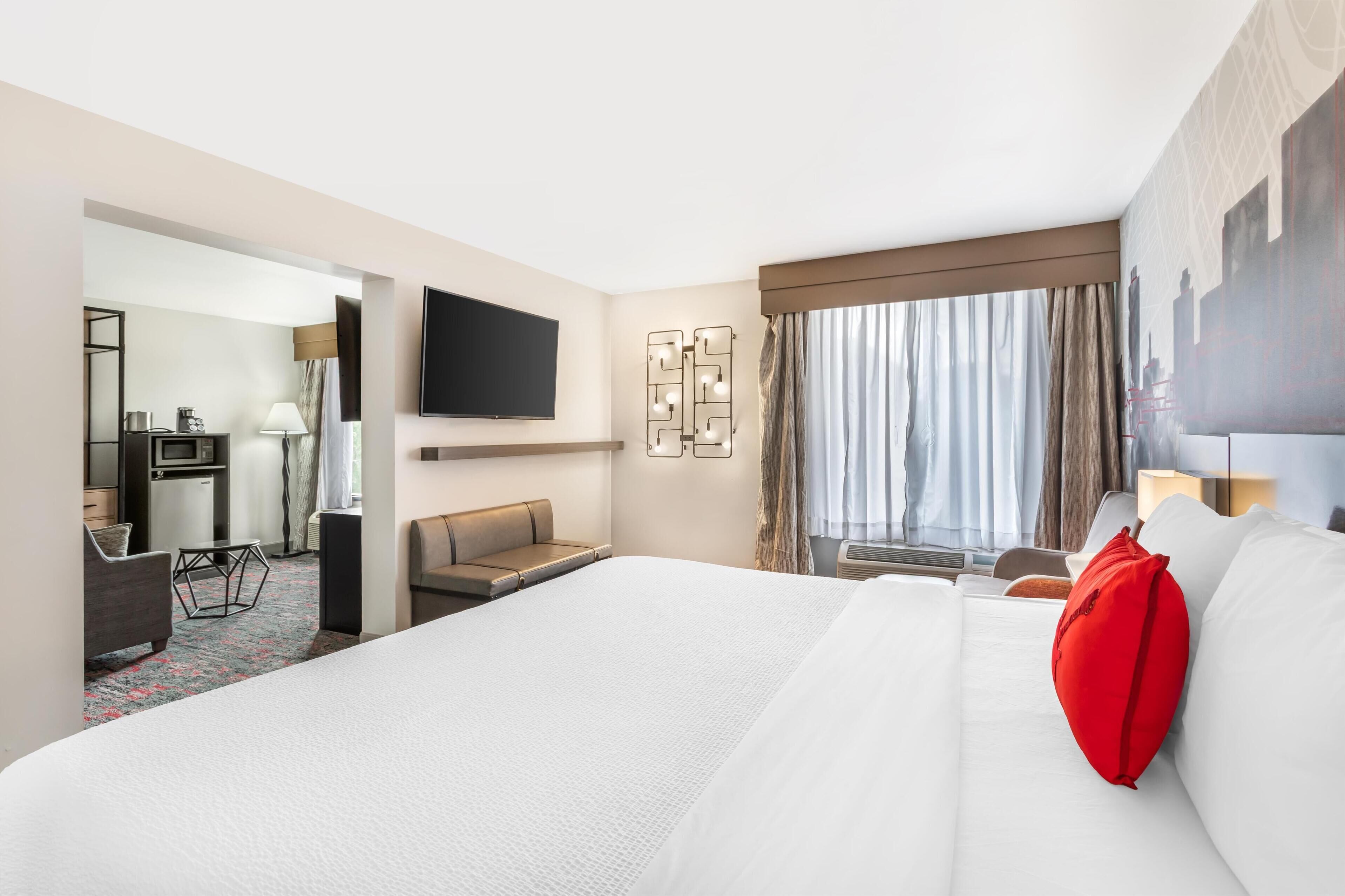 Une chambre d’hôtel avec un grand lit, un bureau, une chaise, une télévision et une fenêtre avec des rideaux.