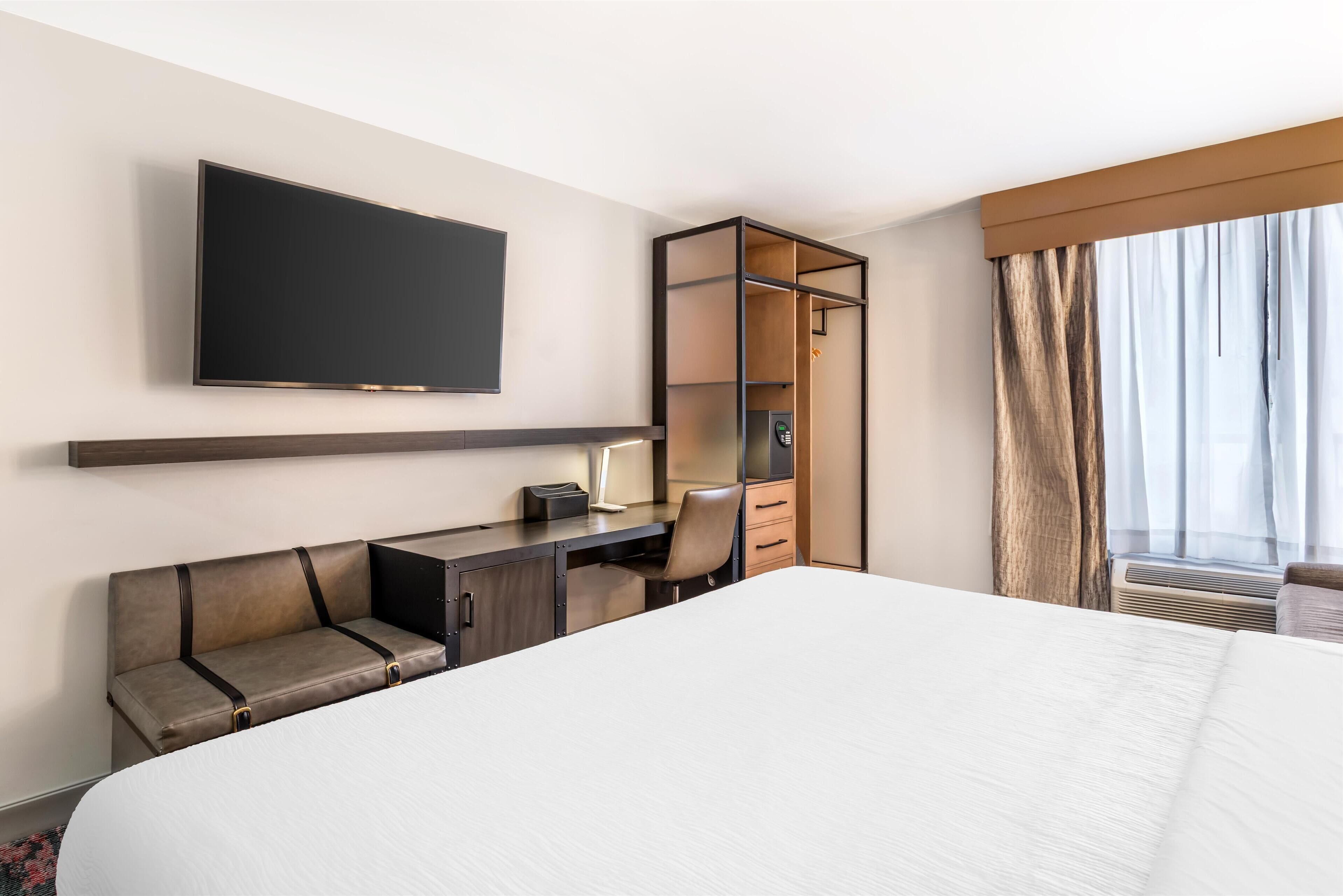 A hotel room with a large bed, a desk with a chair, a television mounted on the wall, and a wardrobe.