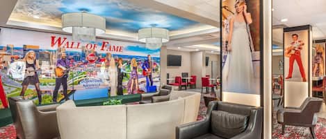 Un hall d’hôtel doté d’une grande fresque murale représentant un « mur de la gloire », de sièges confortables et d’un lustre moderne.