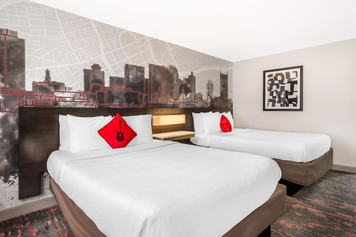 A hotel room with two beds, a cityscape mural on the wall, and a framed artwork.
