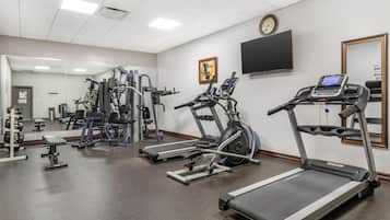 Un gimnasio con cintas de correr, máquinas de pesas y un espejo.