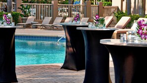 A poolside area with lounge chairs and round tables, some with flower arrangements. - Renaissance Orlando Airport Hotel by Marriott (Orlando)